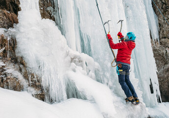 Ice climber dressed in warm winter climbing clothes, safety harness and helmet climbing frozen...