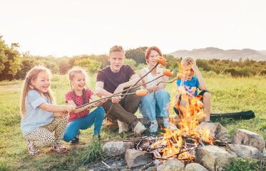 Five kids group Boys and girls cheerfully laughed and roasted sausages on sticks over a campfire...