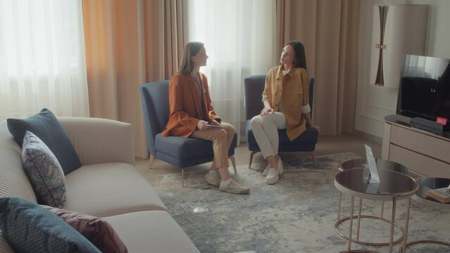Zoom in shot of female customer service assistant and potential buyer sitting on armchairs on mock-up living room in furniture store