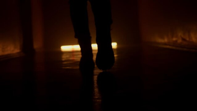 Silhouette of feet in winter boots walking along a dark corridor. Orange light.