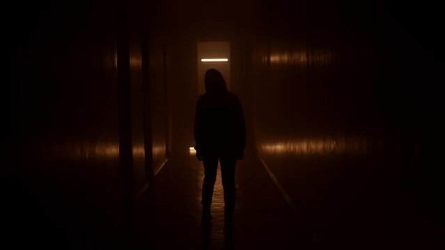 Silhouette woman walks along a dark corridor. Orange light.