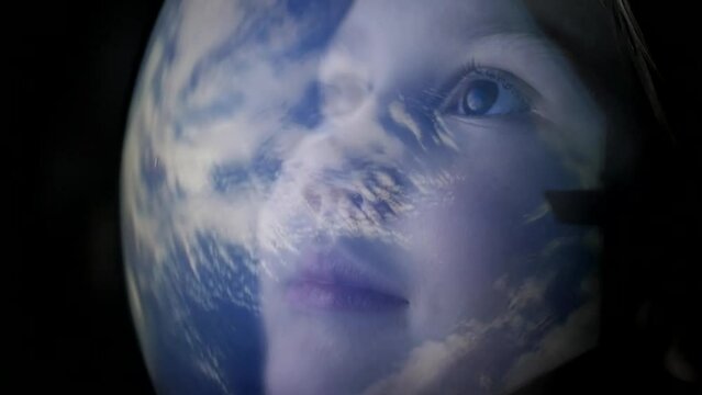 A happy, surprised child in a spacesuit helmet looks at planet earth from space with his eyes wide open. Childhood dream of becoming an astronaut. Space through the eyes of children