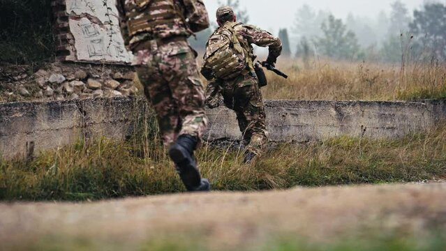Military Detachment Jumps Over a Concrete Wall and Goes Behind a Ruined House