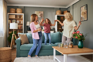 Overjoyed three generations of women dancing together in living room