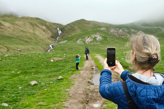 Unrecognizable mother taking photos and recording video of family members on vacation in mountainous countryside