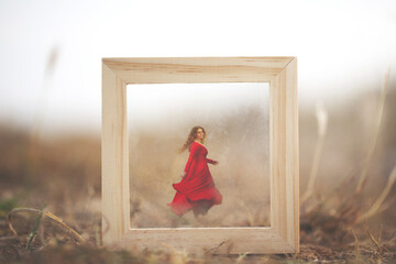 woman dressed in red running away through a surreal frame in the middle of nature