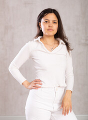 Studio portrait of pretty young Asian girl in a white trouser suit on a gray background