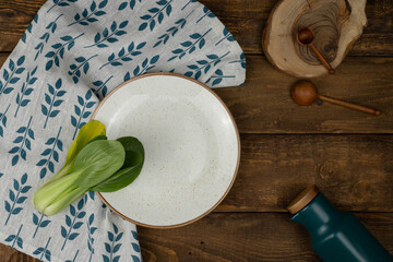 Pak choi cabbage laying on white plate on wooden brown background with wooden spoons and utensils...