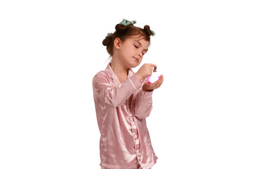 Cute little girl with curlers in pink silk pajamas on a white background is wearing perfume