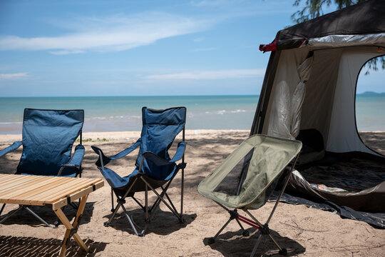 Camping setup on the beach, Chairs, picnic table, and a tent with a campfire. Relish in family moments and the beauty of the sea at sunrise. Nature is an endless source of joy.