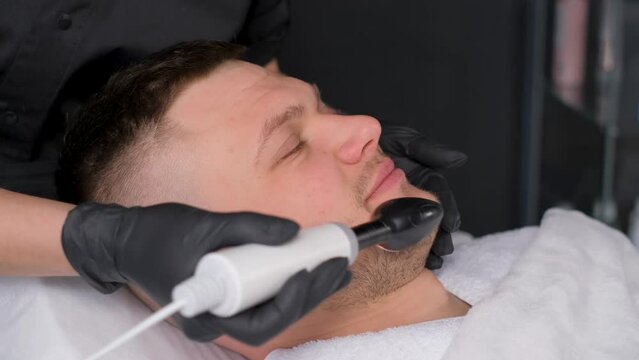 Close-up of a bearded man enjoying a radio frequency facelift at a beauty clinic.