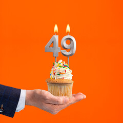 Hand holding birthday cupcake with number 49 candle - background orange