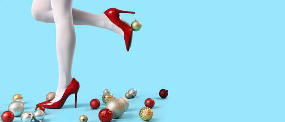 Young woman in high-heels with Christmas balls on blue background with space for text