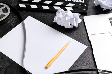 Blank paper sheet with movie clapper and film reel on dark background
