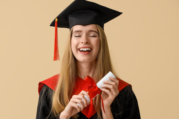 Female graduate student with diploma on beige background, closeup