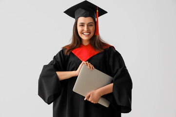 Female graduate student with laptop on light background