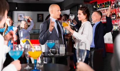 Cheerful smiling male and female colleagues having fun on corporate party in bar