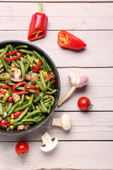 Frying pan with different vegetables on light wooden background