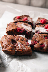 Baking paper with pieces of raspberry chocolate brownie on grey table, closeup