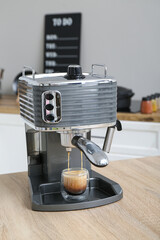 Modern coffee machine with glass of hot espresso on table in kitchen