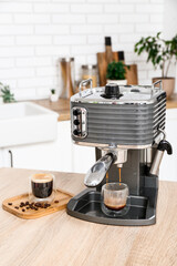 Modern coffee machine with glasses of hot espresso on table in kitchen