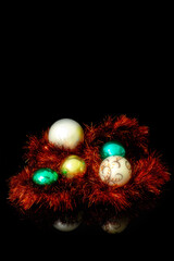 White, golden and and green Christmas baubles nested in a red Christmas tinsel on a black background