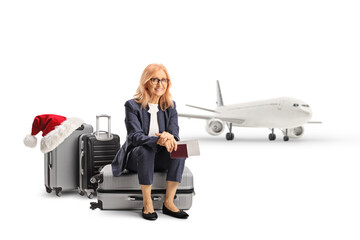 Mature woman sitting on a suitcase with a passport and ticket and waiting for a christmas flight at...
