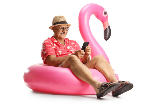 Mature male tourist sitting on a famingo swimming ring and using a smartphone