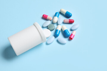 Jar with different scattered pills on blue background