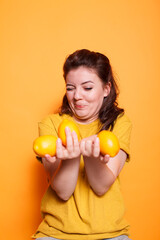 Fototapeta na wymiar In the studio, female individual with a goofy face holding yellow citrus fruits. Young woman displaying a bunch of fresh raw natural lemons for a vitamin rich snack.
