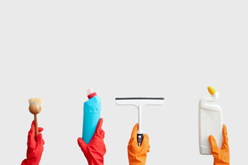 Female hands in rubber gloves holding cleaning supplies on beige background