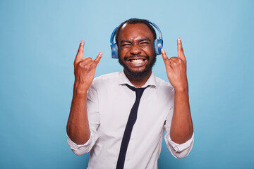 Enthusiastic young man full of energy doing rock and roll hand sign while listening to music in...