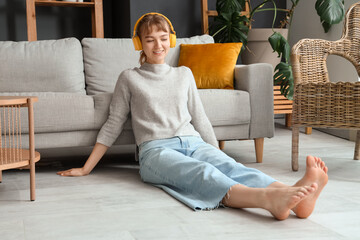 Young woman in headphones sitting on floor with heating at home