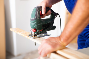 Cropped view of man using a jigsaw machine on wooden plank at home