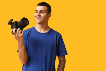 Portrait of male photographer with modern camera on yellow background