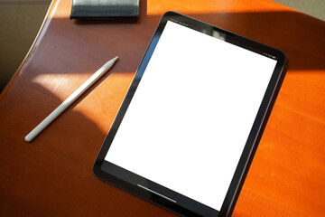 top-down view of a blank tablet on top of a wooden table with a digital pencil next to it
