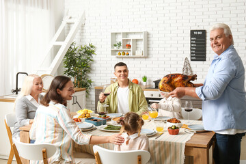 Mature man bringing turkey at festive table with his family on Thanksgiving Day