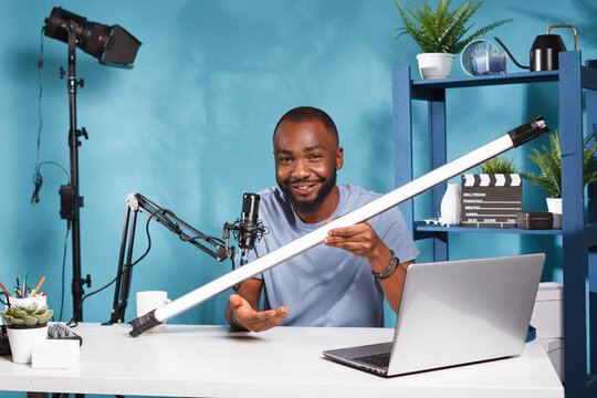 Smiling videographer showing lightning tube while reviewing professional equipment on online blog. African american vlogger testing and recommending led lamp and broadcasting live
