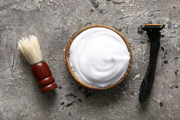 Bowl of shaving foam with brush and razor on grunge grey background