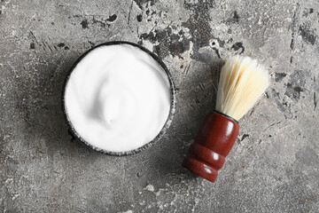 Bowl of shaving foam with brush on grunge grey background