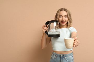 Beautiful young woman with modern electric kettle and cup on beige background