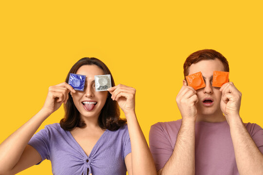 Funny young couple with condoms on yellow background. Safe sex concept