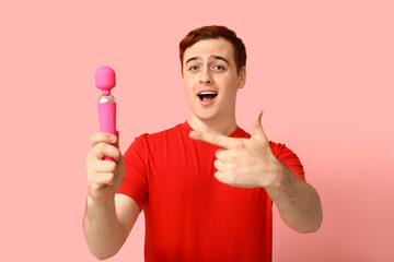 Handsome young man pointing at vibrator on pink background