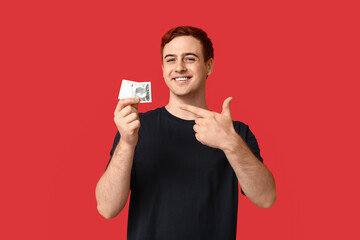 Young man pointing at condoms on red background. Safe sex concept