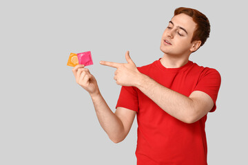 Young man pointing at condoms on grey background. Safe sex concept
