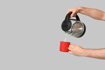 Man pouring hot water from modern electric kettle into mug on grey background
