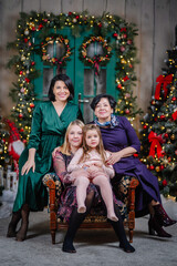 Three generations gather on the Christmas sofa – grandmother, daughter, and granddaughters,...