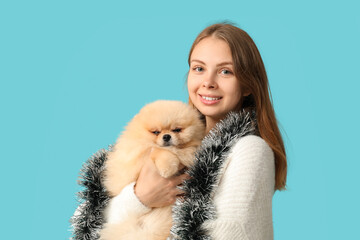 Young woman with cute Pomeranian dog and Christmas tinsel on blue background