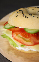 Close up of bagel with vegan cheese, fresh vegetables on wooden plate