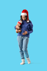 Fototapeta premium Pregnant African-American woman in Santa hat with toy bear on blue background